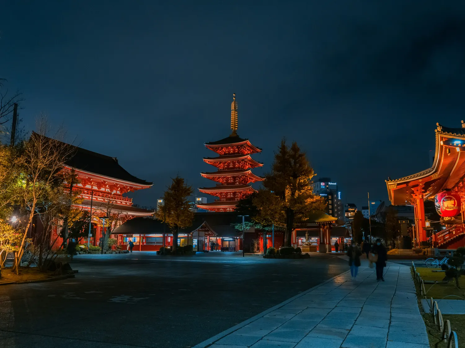 Senso-ji at blue hour: the five-storey pagoda and Hozomon lit against a deep blue sky, the plaza almost empty.