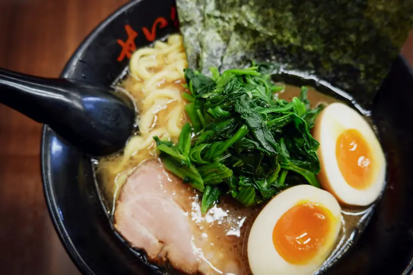 A bowl of ramen with nori, greens, chashu and a soft egg.