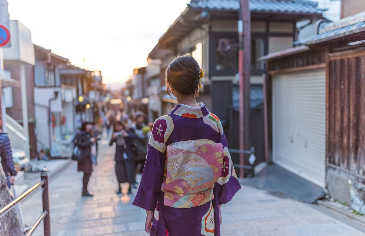 A woman in kimono walking down a narrow old street of wooden townhouses at golden hour.