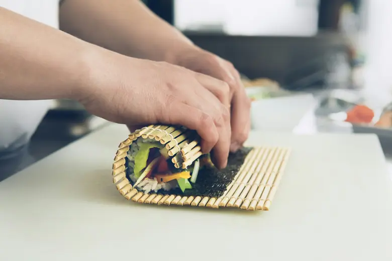 Two hands rolling sushi on a bamboo mat.