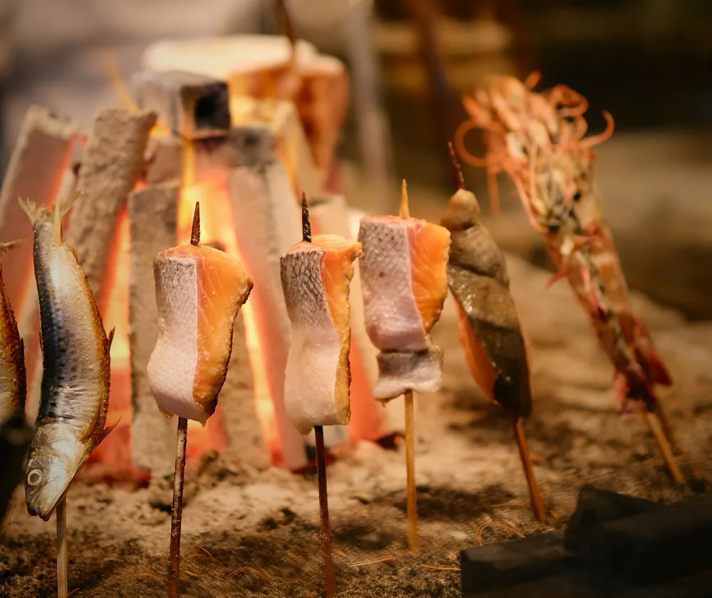 Fish and prawns on skewers set around a charcoal hearth at a robatayaki counter.