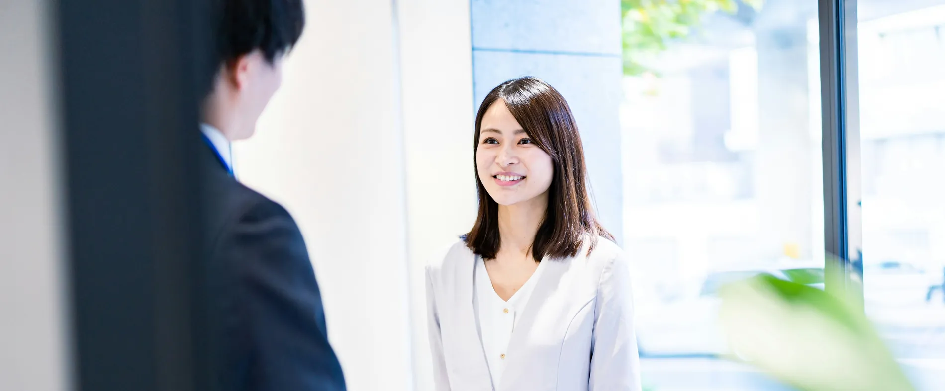 A guest arriving with a suitcase is greeted at the entrance by a member of staff.